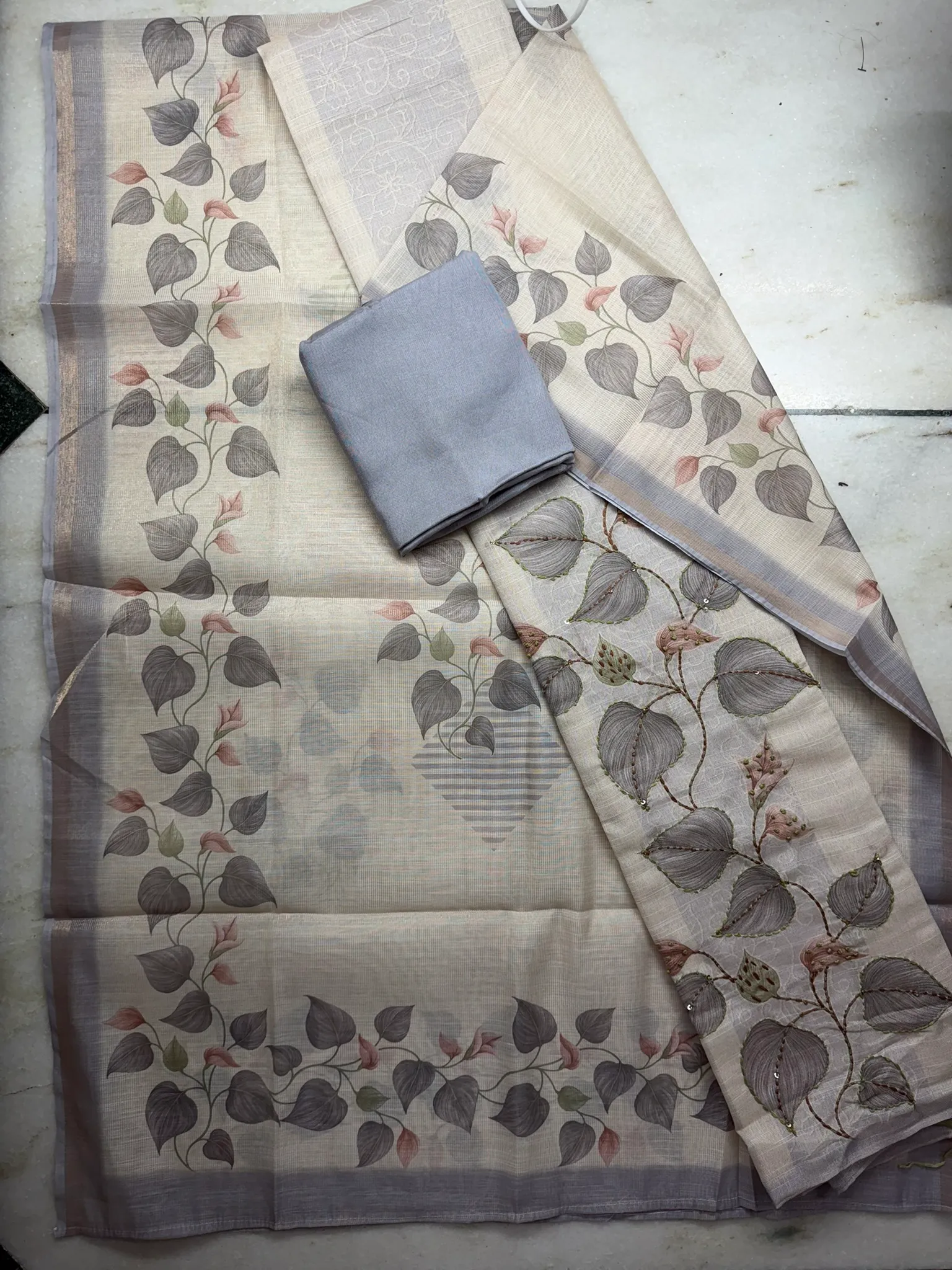 The unstitched set — the printed-and-embroidered kurta panel, a steel-grey bottom, and the leaf-bordered dupatta.