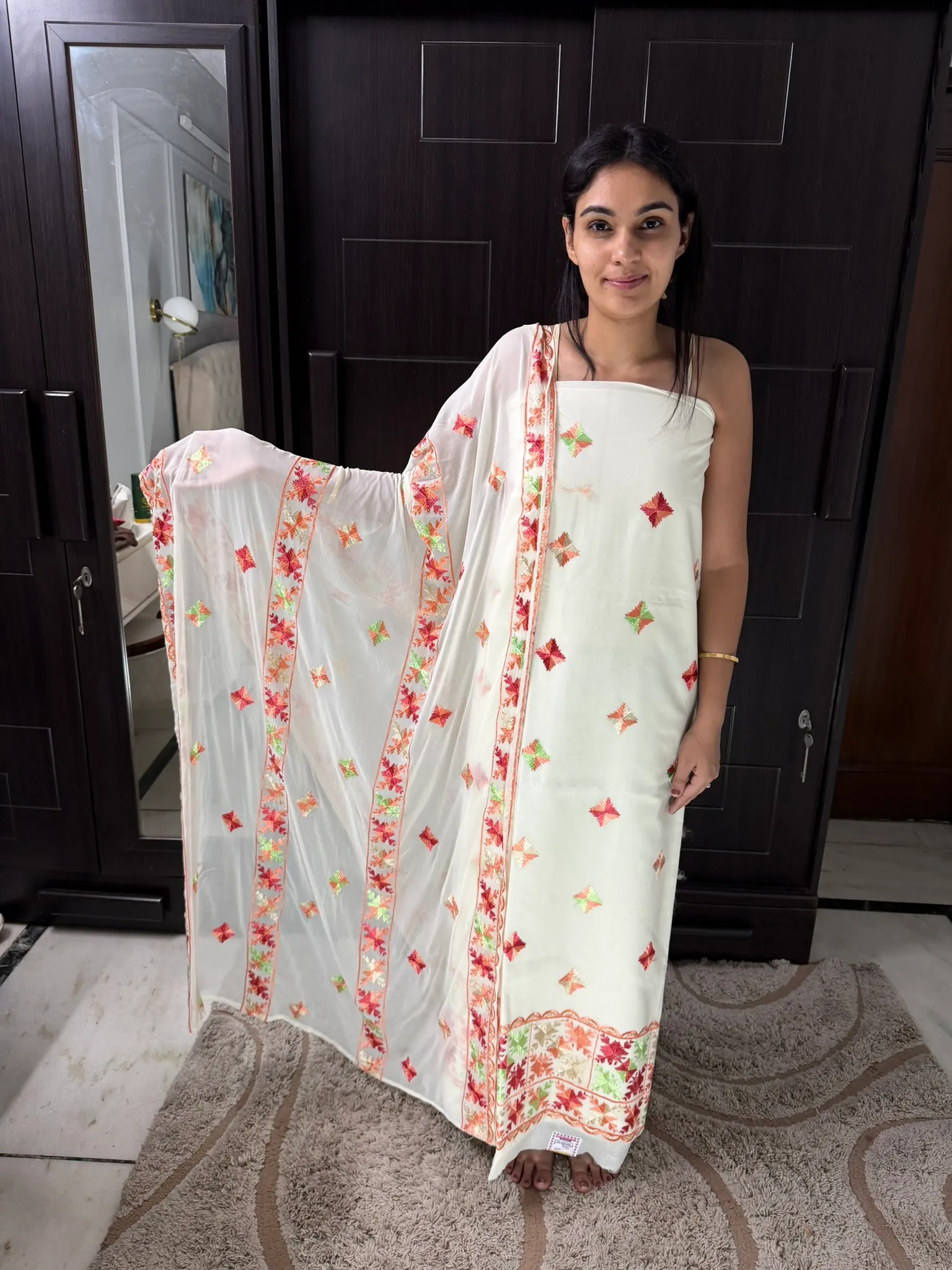 The unstitched set held to the light — butis scattered across ivory, the dupatta bordered in colour.