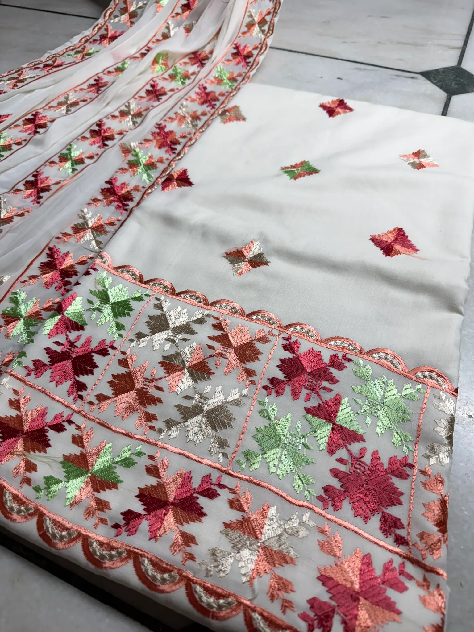 The banded hem, worked in coral, wine and green darning stitch with a scalloped edge.