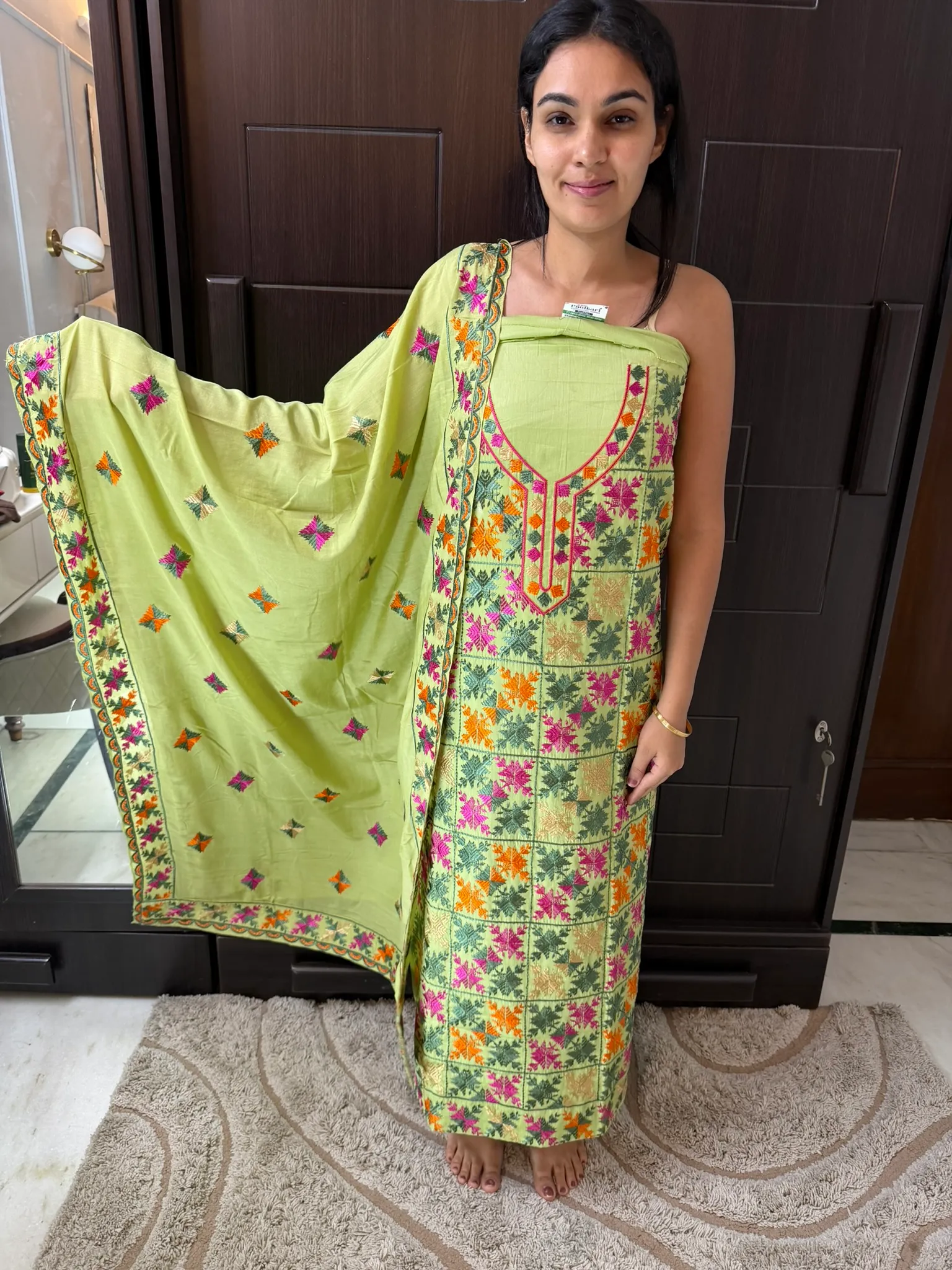 The unstitched set held to the light — the kurta panel almost solid with thread, the dupatta scattered with butis.